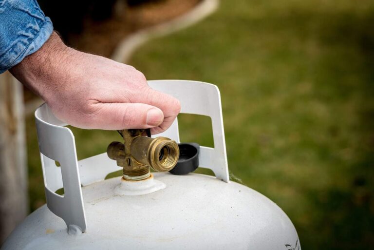 A homeowner checks the percentage gauge on a residential propane tank in a grassy backyard.