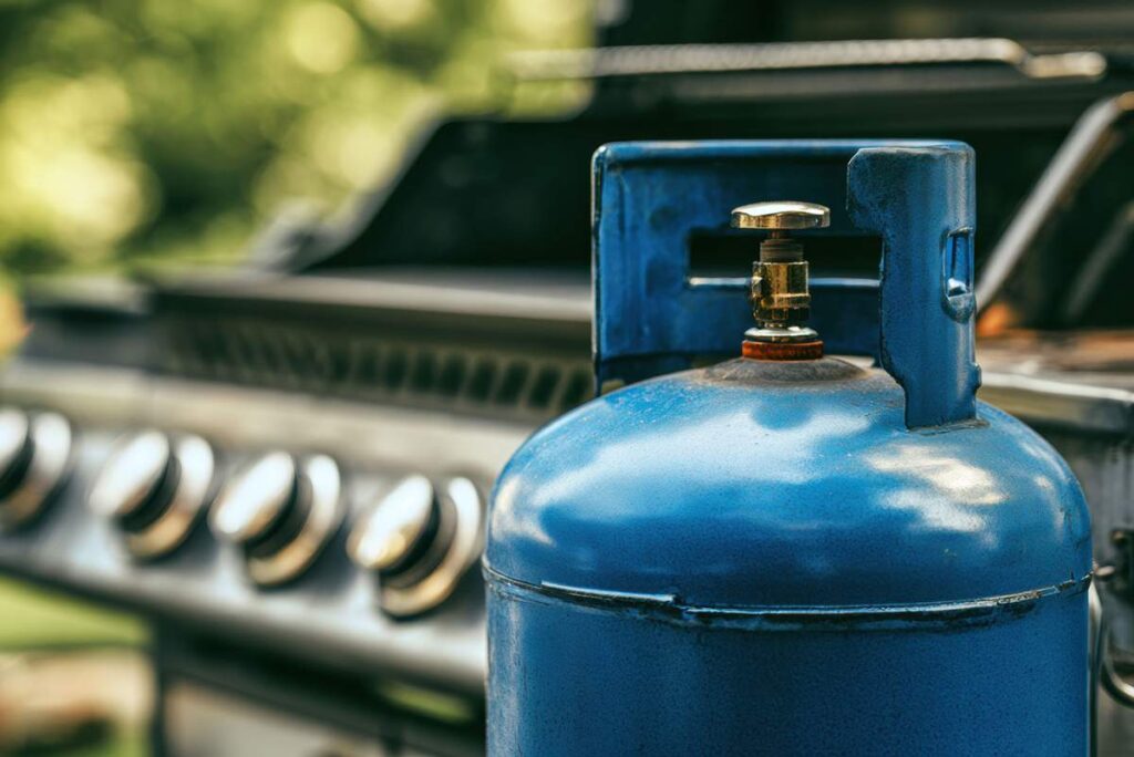 A full 20-pound propane cylinder beside a gas grill and outdoor patio heater.